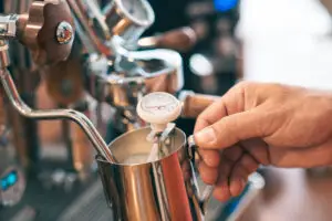 Barista is using temperature tool to prepare milk in milk frother. coffee temperature